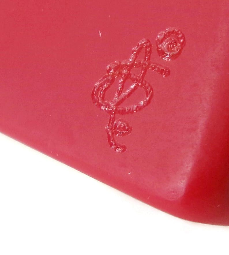 May include: Close-up of a red object with a stylized, embossed design. The design appears to be a musical note or a stylized letter. The object has a smooth, glossy surface.