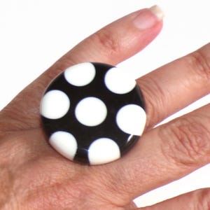Puede incluir: Un anillo grande y redondo con base negra y lunares blancos. El anillo es una pieza llamativa, con un acabado brillante y un patrón clásico. El anillo es un accesorio divertido.