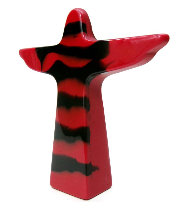 May include: A red and black abstract sculpture with a cross-like shape. The sculpture has a solid red base and a body with horizontal black stripes. The arms extend outward, creating a unique and modern design.