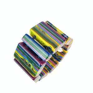 May include: A colorful bracelet composed of rectangular, striped beads in shades of yellow, green, blue, purple, and pink. The beads are strung together with a black cord, creating a vibrant and eye-catching accessory.