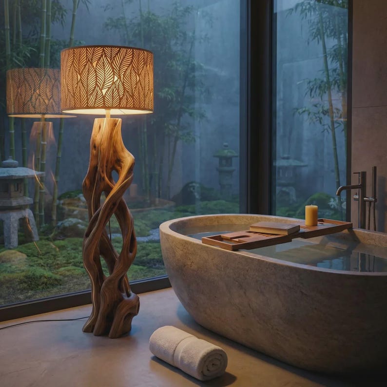 May include: A floor lamp with a natural, twisted driftwood base and a cylindrical lampshade featuring a repeating leaf cutout pattern. The lamp emits a warm glow, standing beside a stone bathtub with a wooden tray and a rolled white towel.
