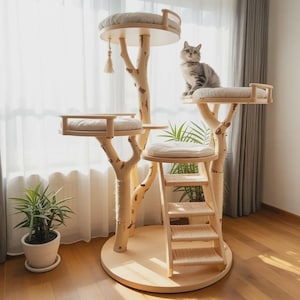 May include: A wooden cat tree with multiple platforms and cream-coloured cushions. The tree has a natural finish, a sisal rope scratching post, and a ladder. A grey tabby cat is perched on one of the platforms. The cat tree is a stylish piece of cat furniture.