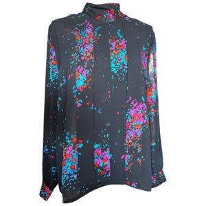 May include: A black long-sleeved blouse with a high collar and colorful abstract splatter design. The pattern includes splashes of blue, pink, orange, and purple. The blouse has pleats down the front and cuffs at the wrists.