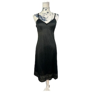 May include: A black slip dress with spaghetti straps and a V-neckline. The dress features a lace trim along the neckline and hem. The dress is displayed on a mannequin.