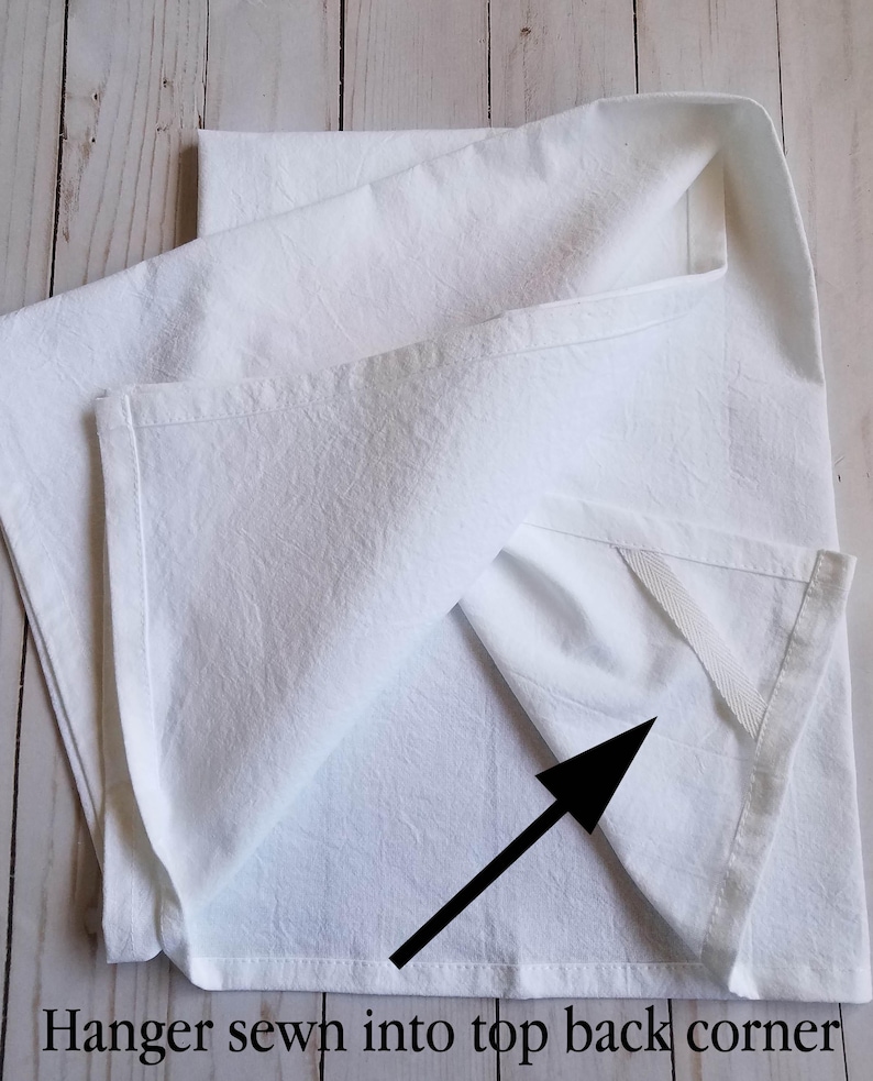 May include: A white kitchen towel with a white fabric hanger sewn into the top back corner.