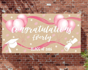 May include: A graduation banner with the words "Congratulations Everly" in white script, pink balloons, and a graduation cap illustration. The banner also includes "Class of 2026" in pink.