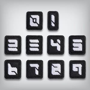May include: A collection of ten black and white embroidered patches. Each patch features a unique white geometric design on a black background. The patches are square or rectangular, with a textured border.