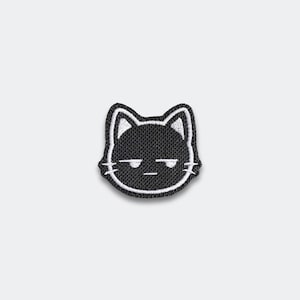 May include: A black and white embroidered patch featuring a cat face with a grumpy expression. The cat's face is outlined in white, with white details for the ears and whiskers. The patch is on a white background.