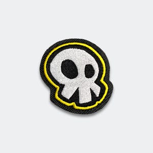 May include: Embroidered patch featuring a white skull with black eye sockets and a jawline, outlined in yellow and set against a black background. The patch is likely for clothing or accessories, adding a touch of edgy style.