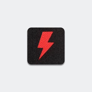 May include: A square-shaped patch with a black fabric base and a red embroidered lightning bolt symbol centered on the surface. The patch features rounded corners and a visible woven texture throughout the black background and the red bolt design.