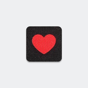 May include: A square-shaped patch featuring a textured black fabric base with a vibrant red heart centered in the middle. The heart design is composed of a dense, woven material that contrasts against the dark background of the square patch.