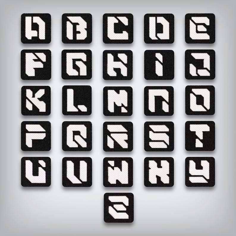 May include: A collection of black square patches, each displaying a white letter of the alphabet in a bold, geometric font. The letters A through Z are represented, with a stylized design. The patches are arranged in a grid pattern against a gray background.