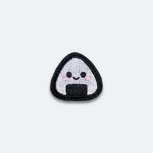 May include: Embroidered patch featuring a smiling onigiri, a Japanese rice ball. The patch has a white rice ball with a black nori seaweed base and border. The onigiri has a cute face with pink cheeks.