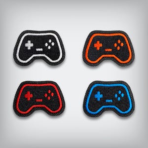 May include: Four black controller patches with colored outlines and button details. The outlines are white, orange, red, and blue. Each patch has a plus sign, minus sign, and four dots.