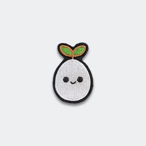 May include: Embroidered patch featuring a smiling, white, seed-like character with two green leaves sprouting from its head. The patch has a black border and is designed with a cute, cartoonish style, perfect for adding to clothing or accessories.
