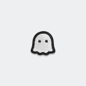 May include: A small embroidered patch in the shape of a ghost. The ghost figure is white with two black circular eyes and is outlined by a thick black border. The embroidery features a textured thread pattern throughout the entire shape.