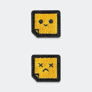 May include: Two square embroidered patches featuring a yellow sticky note design with a black border and a folded corner. The top patch displays a smiling face with two black dots for eyes, while the bottom patch shows a sad face with X-shaped eyes.