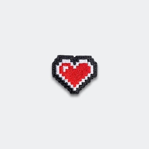 May include: A pixelated heart patch with a red center, white accents, and a black border. The heart shape is reminiscent of classic video game graphics. This patch is suitable for clothing or accessories.