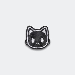 May include: Embroidered patch featuring a black cat face with an angry expression. The cat's face is outlined in white, with white details for the ears and eyes. The patch is likely for clothing or accessories.