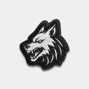 May include: Embroidered patch featuring a snarling wolf head in white against a black background. The patch has a black border and is likely designed to be sewn or ironed onto fabric. The wolf's teeth are bared.