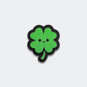 May include: A green four-leaf clover patch with a black border. The clover has a smiling face and is centered on a white background. This embroidered patch is perfect for adding to clothing or accessories.