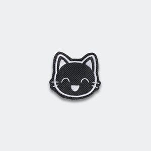 May include: A black and white embroidered patch featuring a smiling cat face. The cat's face is black with white details for the ears, eyes, and mouth. The patch has a white border.
