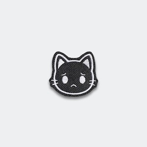 May include: A black embroidered patch featuring a cat face with white accents and a sad expression. The cat's face has white eyes, whiskers, and ear details. The patch is likely for clothing or accessories.