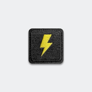 May include: A square, black embroidered patch featuring a yellow lightning bolt design. The patch has a black border and is set against a white background. The lightning bolt is centered and takes up most of the patch.