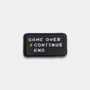 May include: A black rectangular patch with white pixelated text that reads "GAME OVER", an orange triangle, "CONTINUE", and "END". The patch has a black border.