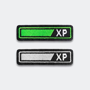 May include: Two rectangular patches with a black border. The top patch has a green bar and the letters "XP" in white. The bottom patch has a white bar and the letters "XP" in white. The patches are on a white background.