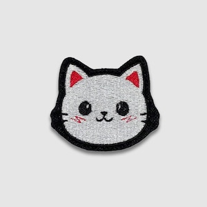 May include: Embroidered patch featuring a cartoon cat face. The cat has a white face with black eyes, a black outline, and red accents on the ears and cheeks. The patch is designed for application on clothing or accessories.