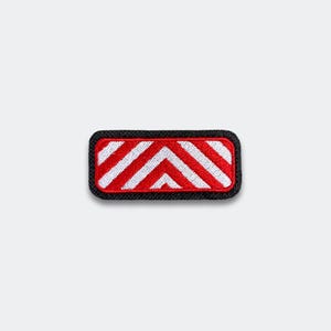 May include: A rectangular patch with a black border. The patch features a red background with white chevron stripes. The design is a simple, geometric pattern, suitable for clothing or accessories.