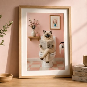 Peut inclure: Une impression d'art encadrée représentant un chat siamois assis sur des toilettes blanches, lisant un journal intitulé Daily News. La scène se déroule dans une salle de bain aux murs roses, sol à damier, étagère en bois et cadre décoratif.