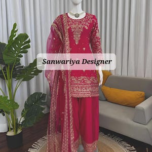 May include: A vibrant fuchsia salwar kameez ensemble on a mannequin. The outfit features intricate gold embroidery on the long-sleeved top, pants, and sheer dupatta. The text "Sanwariya Designer" is displayed on the image.