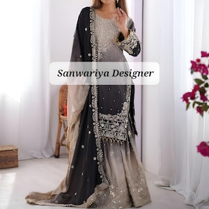 Puede incluir: Un elegante vestido de noche largo hasta el suelo en tonos negro, gris y beige. El vestido presenta intrincados bordados y adornos, con una chal a juego. El texto "Sanwariya Designer" se muestra en la parte delantera.