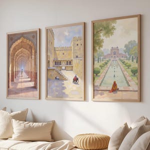 May include: Three framed art prints depicting Indian architecture and landscapes. The artwork features detailed paintings of archways, forts, and gardens with figures. The frames are light-colored wood, and the overall aesthetic is warm and inviting.
