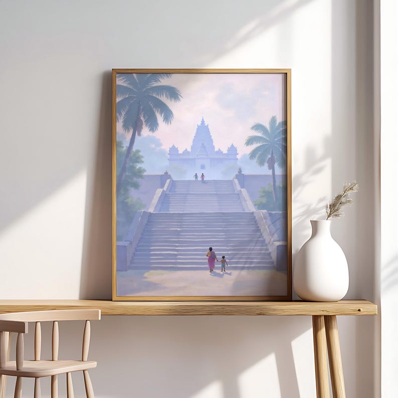 May include: Framed art print depicting a temple with a grand staircase, palm trees, and figures ascending. The artwork is in a gold frame and rests on a wooden surface. A white vase with dried plants sits nearby, adding a touch of decor.