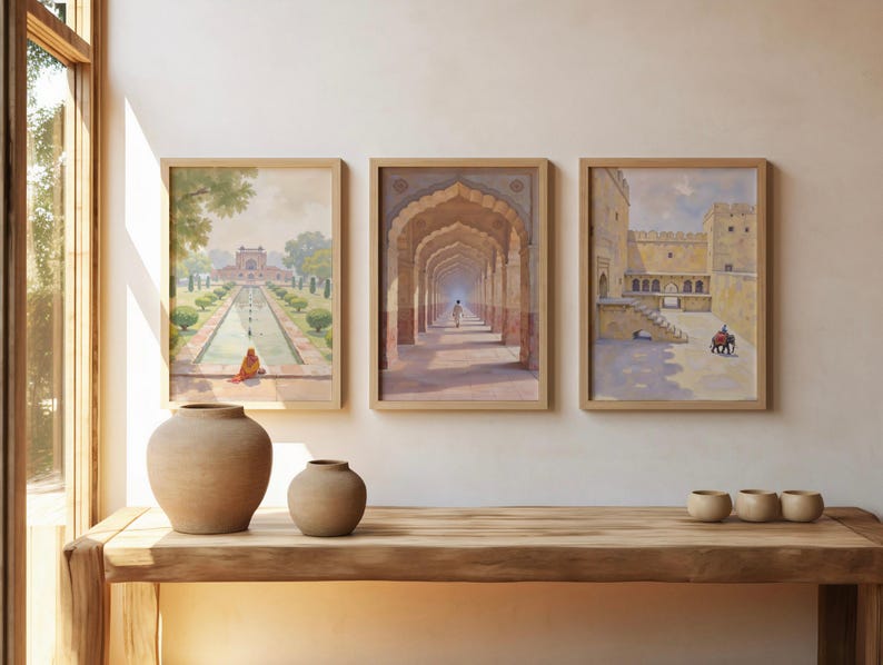May include: Three framed watercolor prints depicting Indian architecture hang above a wooden table. The prints feature scenes of archways, courtyards, and gardens. Two beige ceramic vases and three small bowls sit on the table.