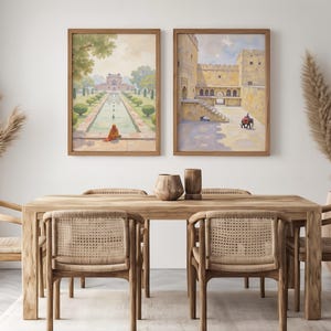 May include: Two framed watercolor paintings of Indian architecture hang above a wooden dining table with six woven chairs. The paintings depict a garden scene and a fortress with figures. Decorative vases and dried plants complete the room.