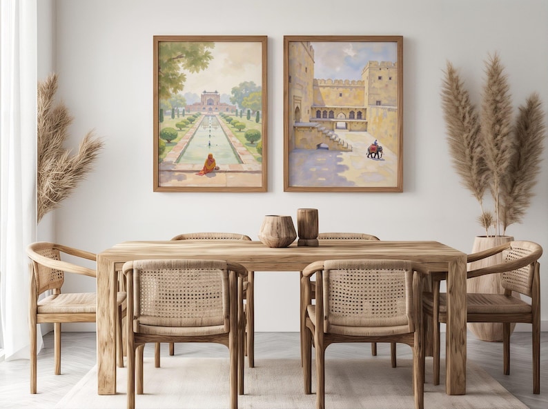 May include: Two framed watercolor paintings of Indian architecture hang above a wooden dining table with six woven chairs. The paintings depict a garden scene and a fortress with figures. Decorative vases and dried plants complete the room.