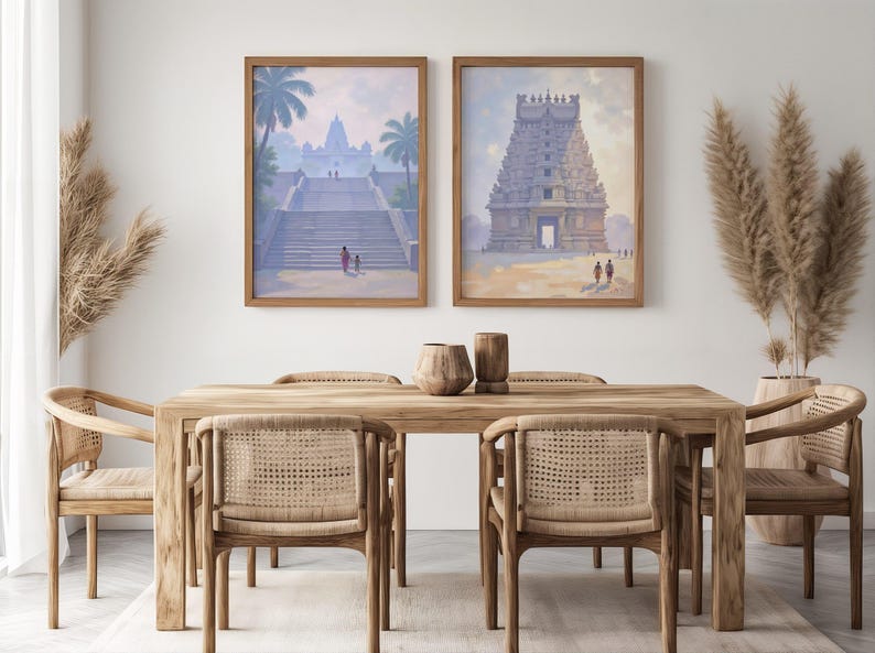 May include: Two framed watercolor prints of Indian temples hang above a wooden dining table with six woven chairs. The artwork features temples with palm trees and figures. Decorative vases and pampas grass complete the scene.