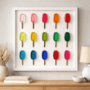 May include: A framed artwork featuring twelve colorful popsicle sculptures. The popsicles are arranged in three rows of four, with a variety of colors including pink, red, orange, yellow, green, and blue. Each popsicle has a wooden stick.