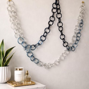 Puede incluir: Decoración mural con diseño de cadena. La cadena está compuesta por grandes eslabones ovalados entrelazados en tonos claros, azules y negros. Se suspende de la pared con ganchos dorados, creando una exhibición artística moderna.