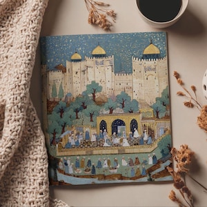 May include: A square art print depicting a Middle Eastern city with a fortress, trees, and figures in traditional dress. The artwork uses blues, golds, and creams, with a starry sky. A cup of coffee and a beige knitted blanket are in the background.