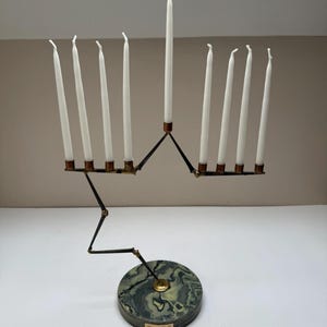 May include: A black and brass menorah with nine white candles. The base is a round, green and gray marble. The menorah has a unique, articulated design.