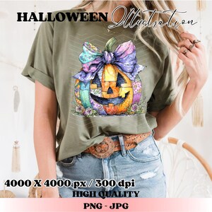 May include: Olive green t-shirt featuring a colorful pumpkin illustration with a large bow. The pumpkin has a smiling face and is decorated with patchwork patterns. Text at the top reads "HALLOWEEN Illustration".
