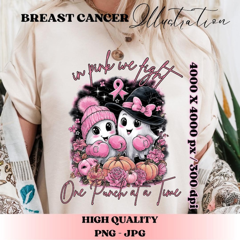 May include: A beige t-shirt with a graphic supporting breast cancer awareness. The design features two cartoon ghosts wearing pink boxing gloves, hats, and surrounded by pink flowers and pumpkins. Text includes "Breast Cancer Illustration", "in pink we fight", and "One Punch at a Time".