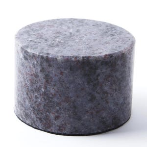 May include: A cylindrical stone paperweight featuring a polished surface with a speckled pattern in shades of gray, blue, and dark red. The object has a flat top and a circular base, showcasing a natural mineral texture throughout its exterior.