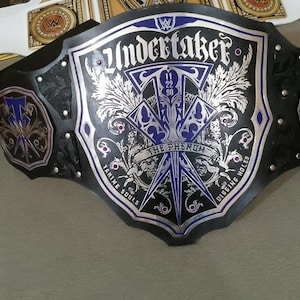 May include: A black and silver wrestling championship belt with the name "Undertaker" and "The Phenom" on the front. The belt has blue accents and the date "11 22 90".