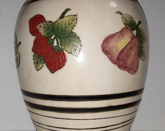 May include: Cream-colored ceramic vase with black stripes and fruit illustrations. The vase features red strawberries, purple pears, and green leaves. The base has a decorative black and blue floral design.